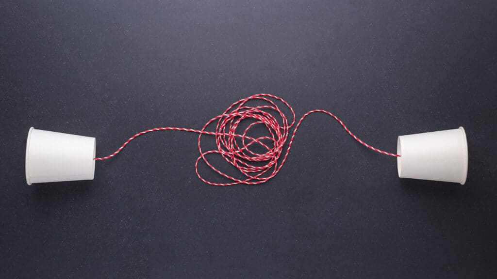 Two white paper cup connect with red rope used for classic phone on black stone table board. For old communication system concept