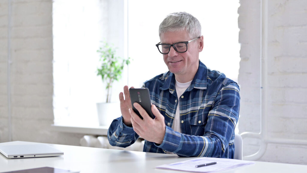 Cheerful Casual Middle Aged Man Using Smartphone in Office